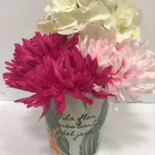 Macetero decorado con flores artificiales de colores blanco, rosa y fucsia, con la frase "La flor más bonita del jardín" impresa en el frontal.